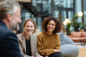 Rencontre conviviale entre un syndic et des copropriétaires dans le hall lumineux d’un immeuble résidentiel.